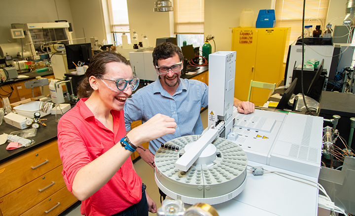 Dr. Scott Simpson looks on as Katharina “Katie” Heitzman, ’22, 一个双化学/生物化学专业的学生使用气相色谱-质谱联用仪(GC-MS)来识别大学化学仪器套件中的化合物.